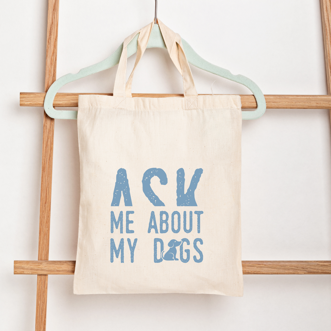 Tote bag with 'Ask Me About My Dogs' text on a wooden rack