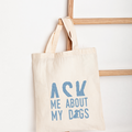 Beige tote bag with blue text 'Ask Me About My Dogs' on a white background
