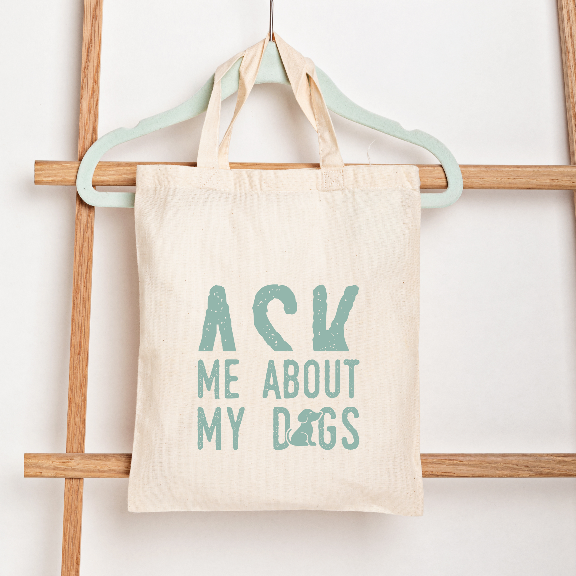Tote bag with 'Ask Me About My Dogs' text on a wooden rack