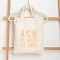 Tote bag with 'Ask Me About My Dogs' text on a wooden rack.