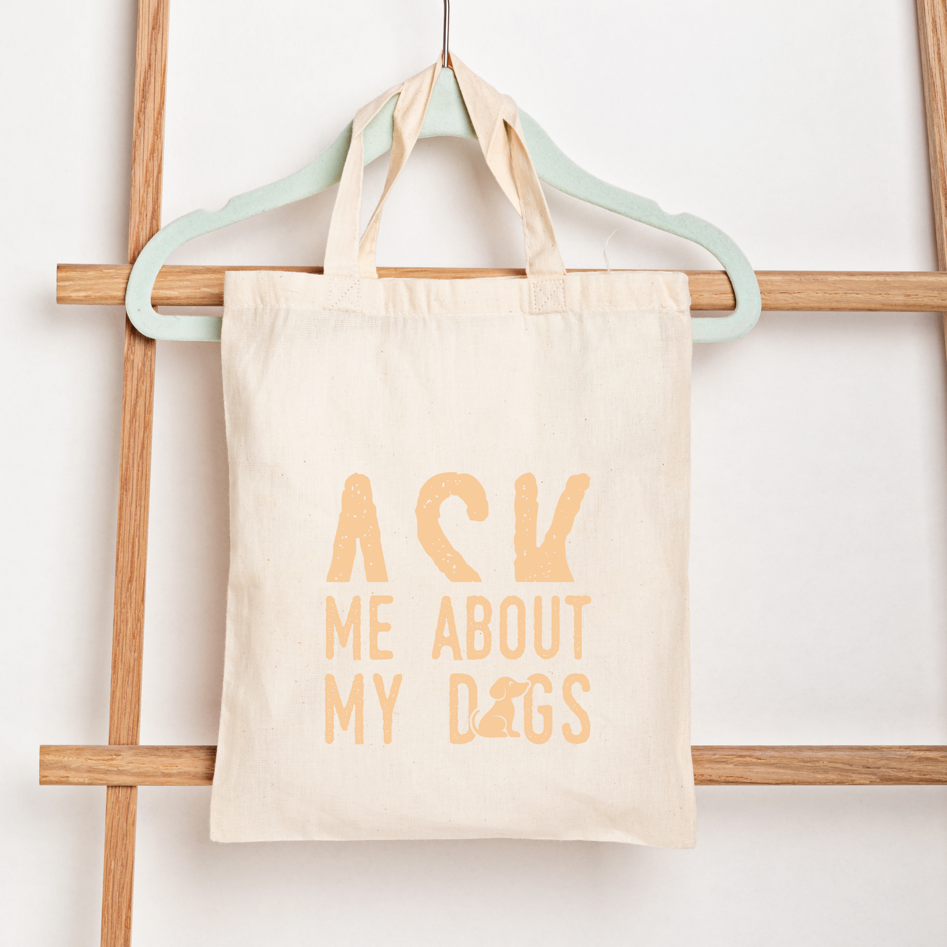 Tote bag with 'Ask Me About My Dogs' text on a wooden rack.