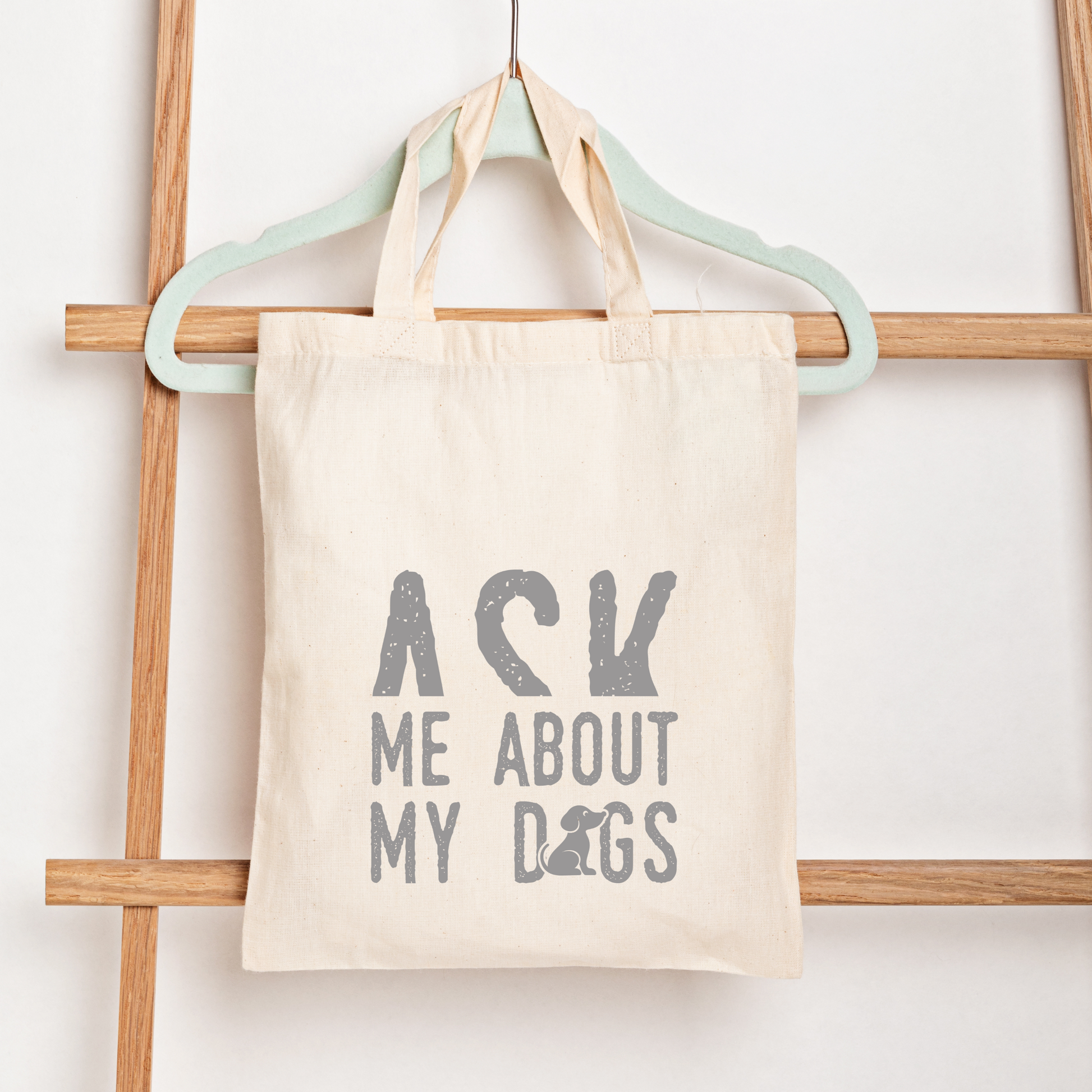 Tote bag with 'Ask Me About My Dogs' text on a wooden rack