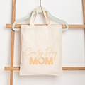 Beige tote bag with 'Crazy Dog Mom' text hanging on a wooden rack.