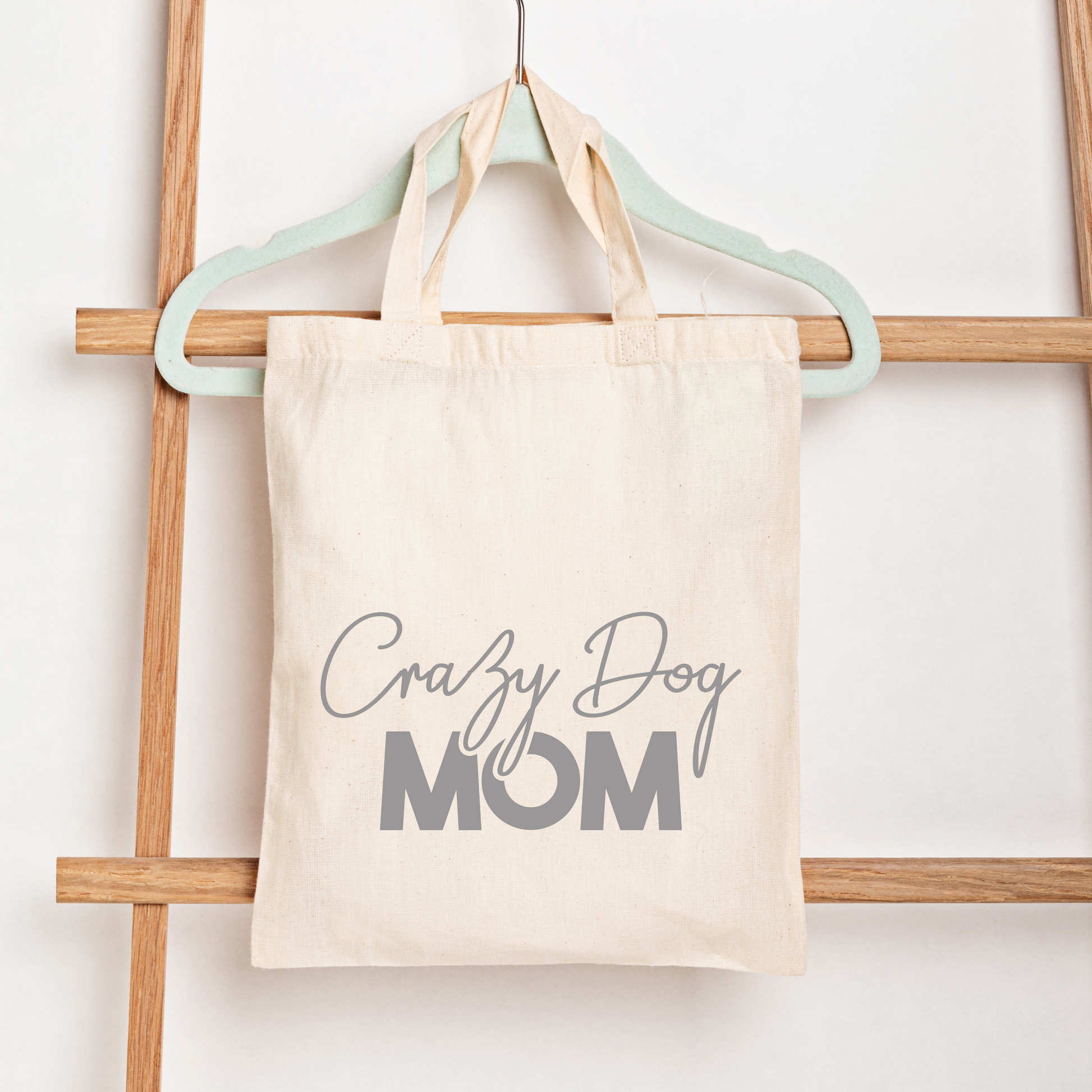 Tote bag with 'Crazy Dog Mom' text hanging on a wooden rack.