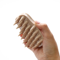 Hand holding a beige silicone brush with pointed ends on a white background