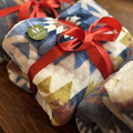Stack of patterned blankets with red ribbons on a wooden surface