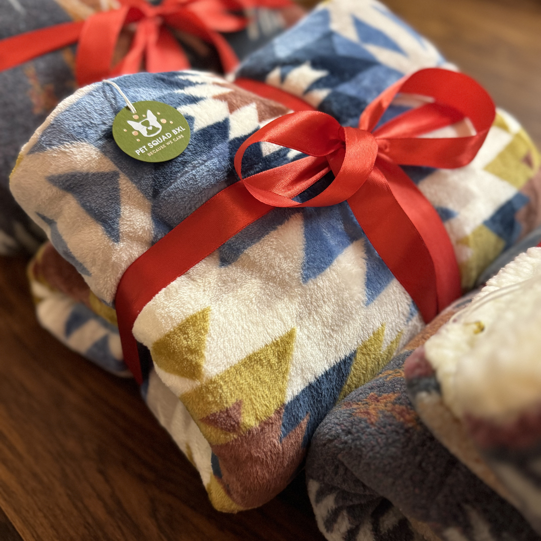 Stack of patterned blankets with red ribbons on a wooden surface