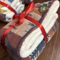 Folded blanket with a red ribbon on a wooden surface, featuring a brand tag.