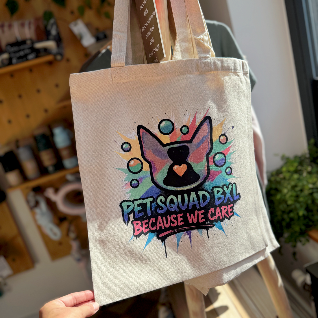 Tote bag with 'Pet Squad BXL Because We Care' design held by a person in an indoor setting.