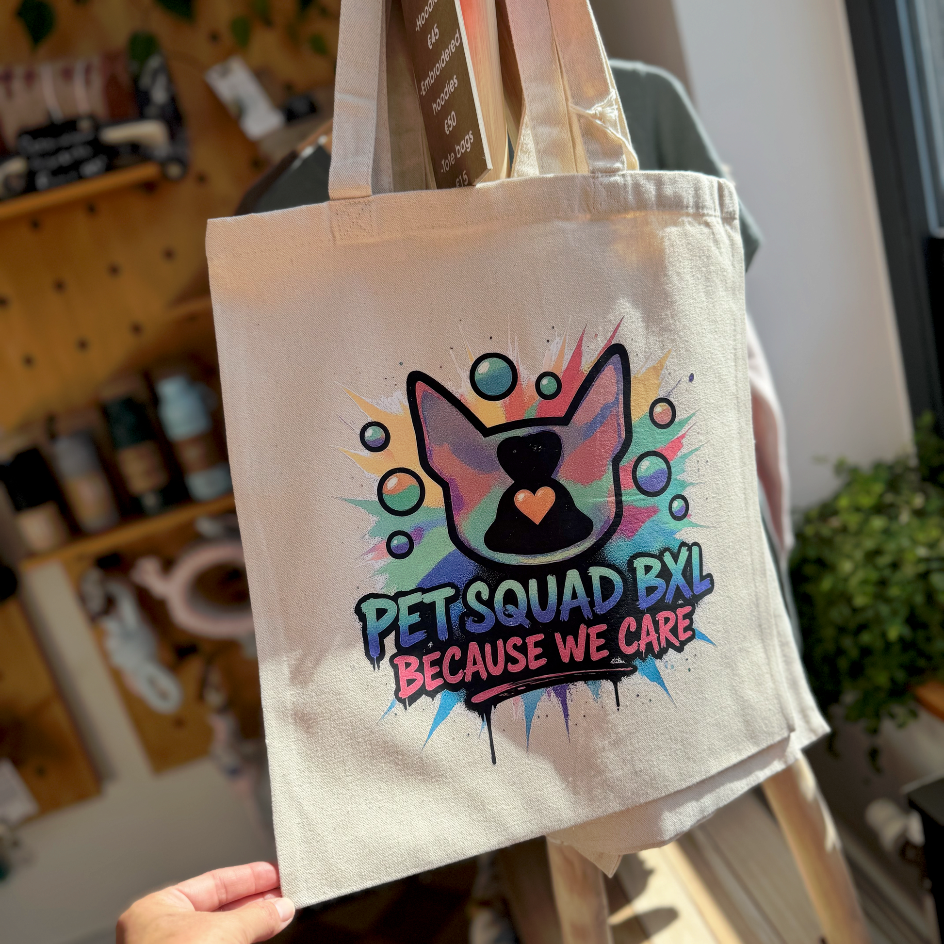 Tote bag with 'Pet Squad BXL Because We Care' design held by a person in an indoor setting.