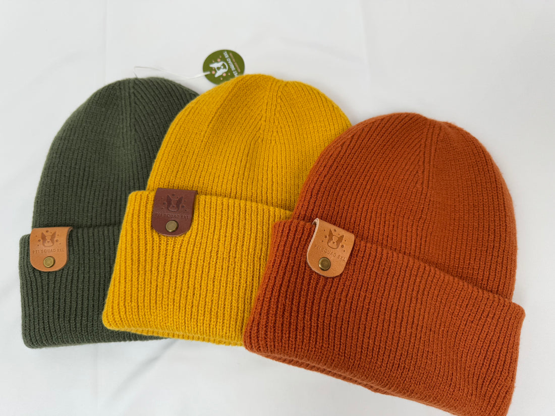 Three knit hats in pink, green, and purple with brand tags on a white background