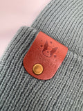 Gray knitted product with a brown leather patch featuring a dog icon and 'PETSQUAD' text.