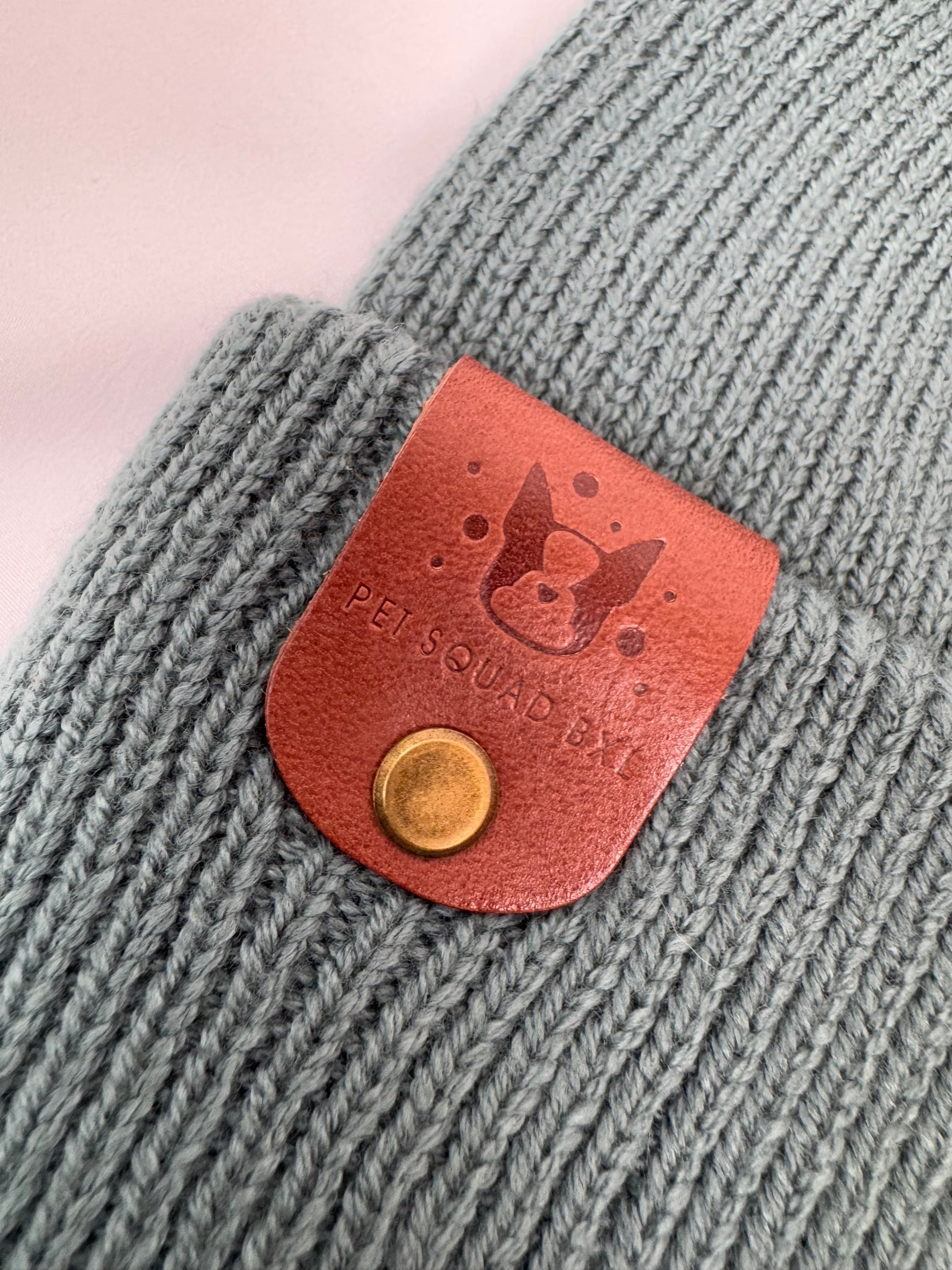 Gray knitted product with a brown leather patch featuring a dog icon and 'PETSQUAD' text.