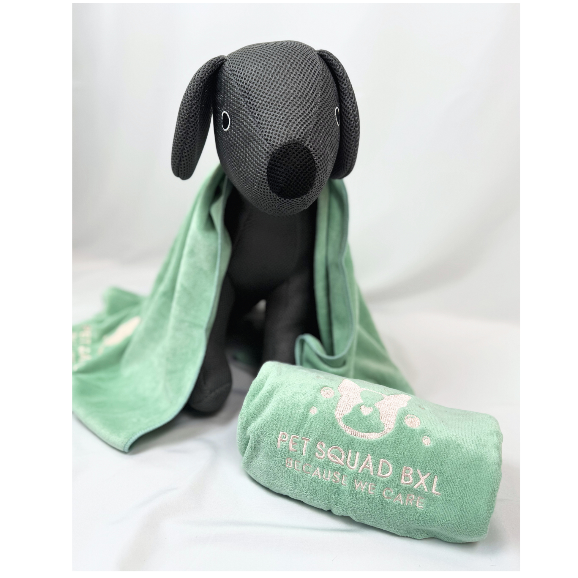 Black dog-shaped pillow with a green towel draped over it on a white background