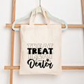 Tote bag with 'Treat Treat Dealer' text on a wooden rack