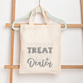 Tote bag with 'Treat Dealer' text hanging on a wooden rack.