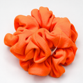 A bright orange fabric scrunchie made of soft fleece or velour material, photographed on a clean white background.