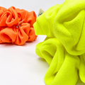 Two plush fleece scrunchies, one bright orange and one neon yellow-green, displayed on a clean white background.