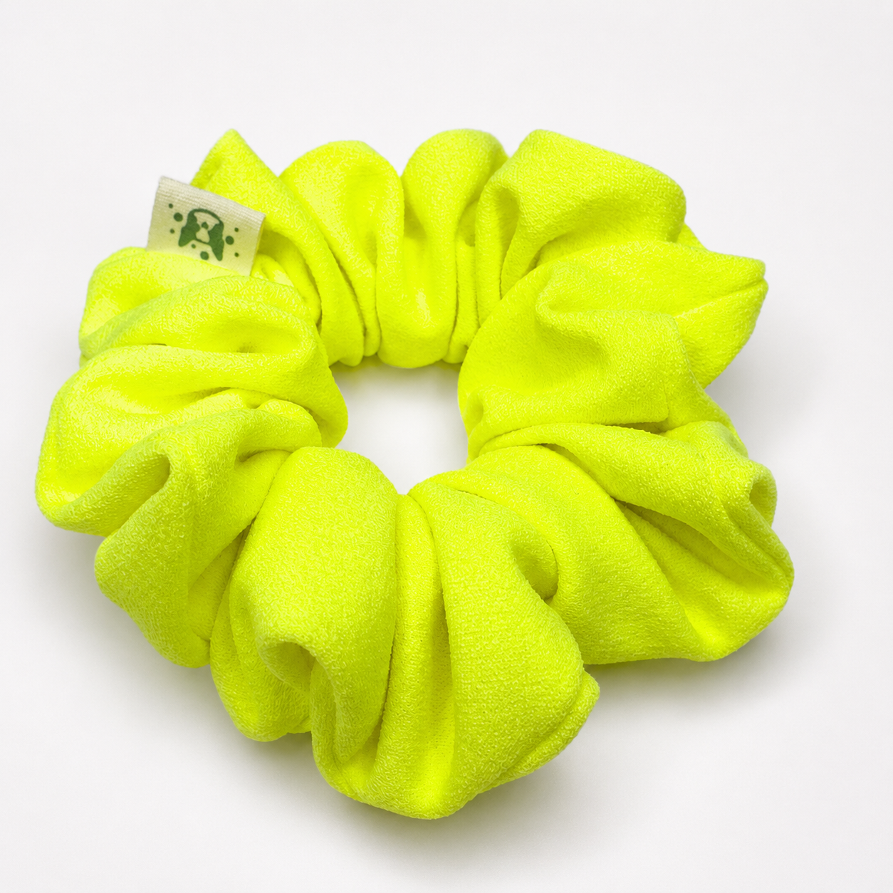 A bright neon yellow-green scrunchie made of plush fleece fabric, shown on a clean white background with a small white brand tag attached.