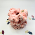 Pink scrunchie with a brand tag on a light background with leaf patterns