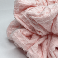 A close-up of a light pink textured fabric accessory, likely a scrunchie or soft hair wrap, showing its waffle-weave pattern on a plain white background.