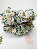 A fabric hair scrunchie with a retro-inspired geometric fan pattern in sage green, dusty pink, and light blue on a white background.